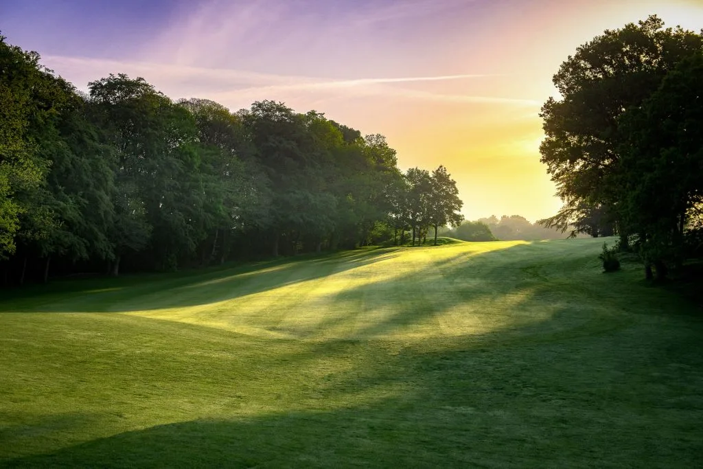 Early morning view of a golf course in Woking with the sun rising over rolling fairways, casting golden light across the dewy grass — perfect for peaceful golf days Woking or early tee times