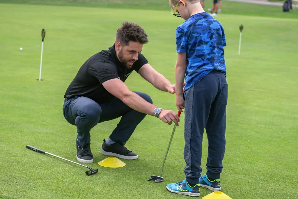 golf coach helping a boy with putting at a junior golf lesson in surrey
