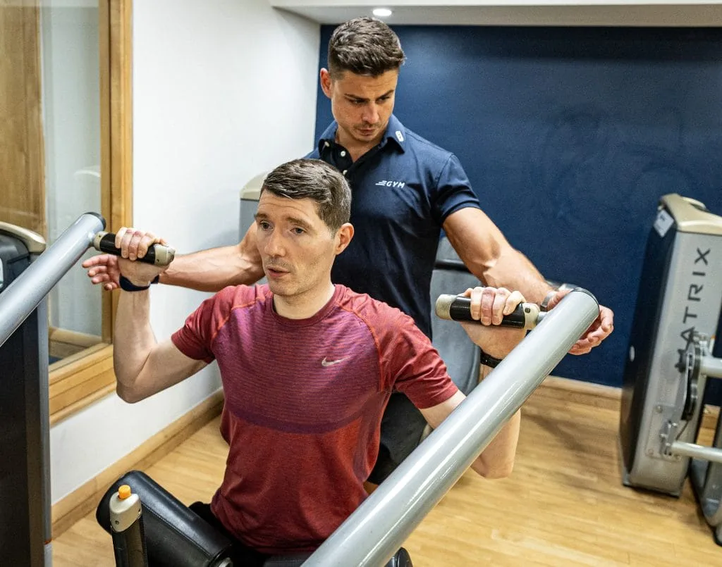 Personal trainer assisting client on shoulder press at gym in Woking